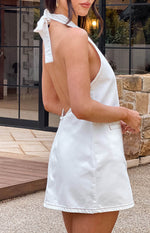 Side view of a white denim halter neck mini dress with an open back, neck tie, and contrast stitching