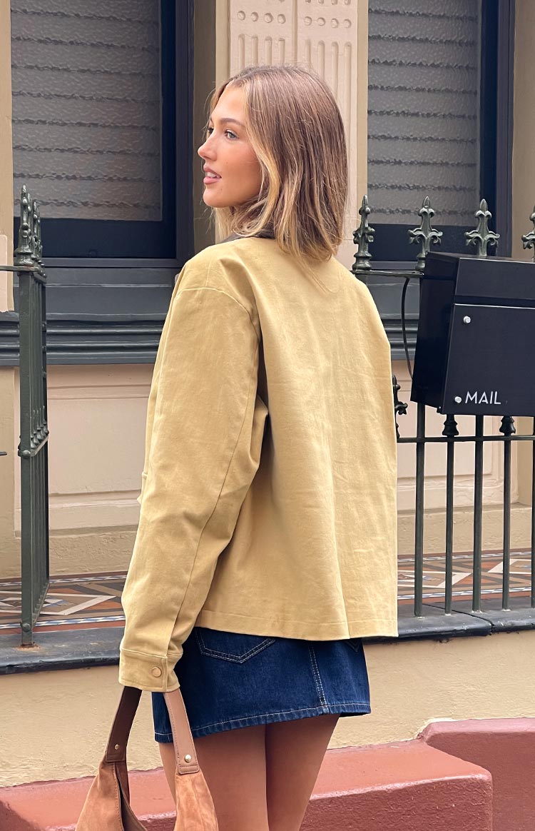 Rear-side view of the cream canvas jacket showing the relaxed fit, long sleeves, and buttoned cuffs