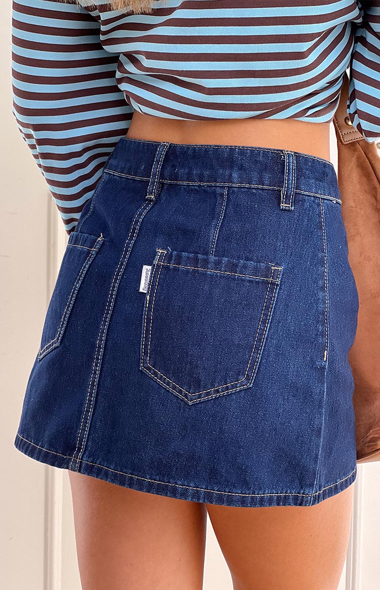 Back view of a dark denim mini skirt with angled back pockets, contrast stitching, and a small white label