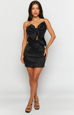 Black strapless mini dress with a large structured bow on the bust, a fitted bodice, and a sleek mini skirt
