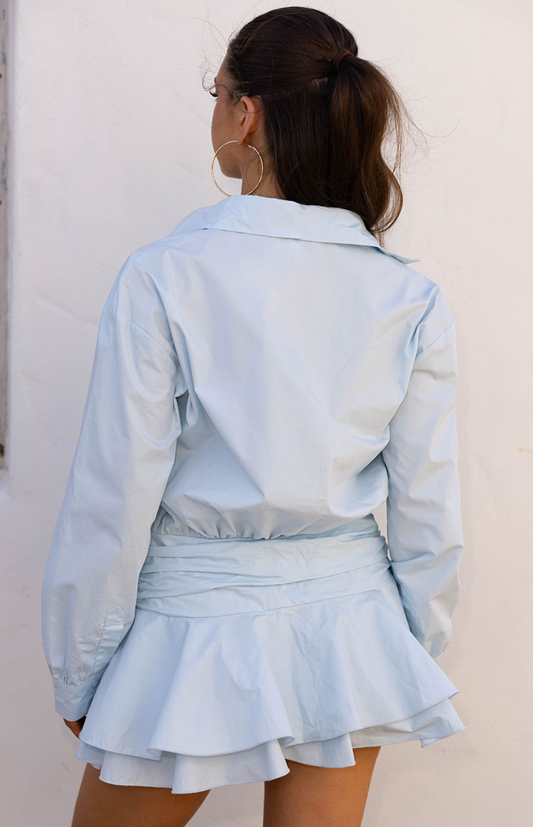 Rear view of a light blue long sleeve mini shirt dress with a gathered elasticated waist and tiered ruffled hem