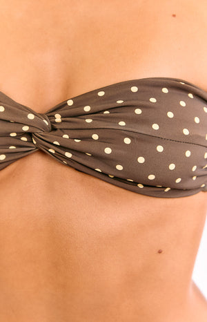 A close-up view of our model showing a brown bandeau bikini top with a small white polka dot pattern and a twisted knot detail in the center.