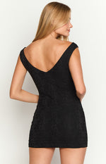 Back view of the black textured mini dress featuring a deep V-neckline and short cap sleeves