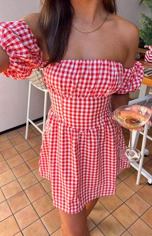 Close-up of the red gingham off-shoulder mini dress showing the shirred bodice and gathered skirt