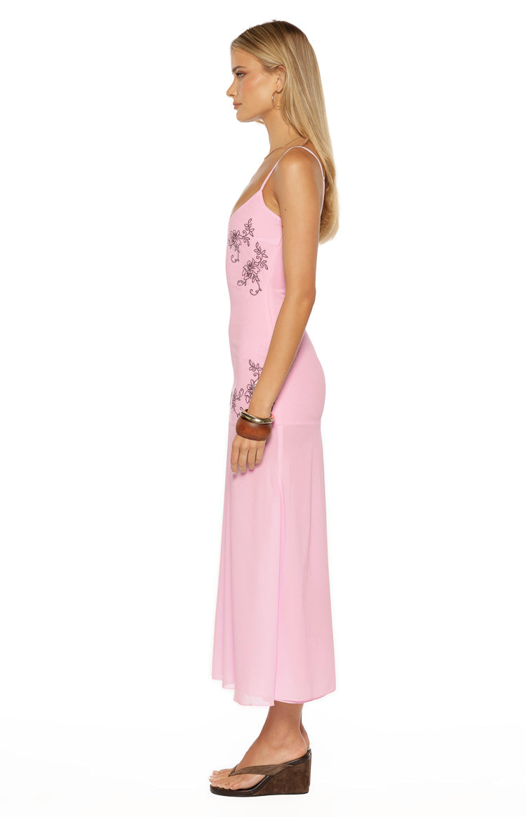 Side view of a light pink midi dress with dark floral embroidery along the side and thin spaghetti straps