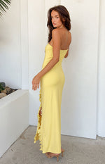 Side view of a yellow strapless maxi dress with a fitted silhouette and a long ruffled slit on the side