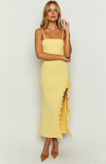 Yellow maxi dress with straight neckline, thin straps, and a high thigh split with ruffles and rosette detail