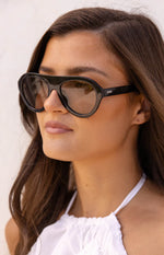 Side profile of black aviator sunglasses with thick frames, dark lenses, and the OTRA logo on the temple