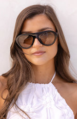 Close-up of black aviator sunglasses with brown lenses, featuring a bold top bar and subtle cat-eye shape