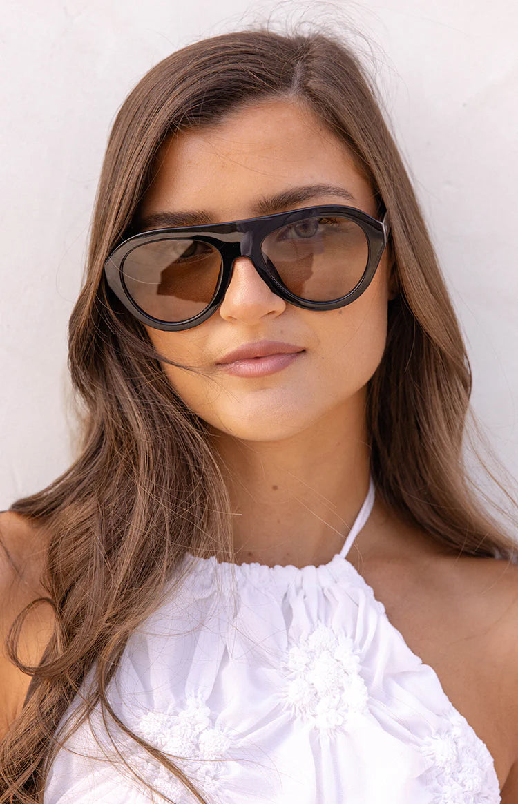 Close-up of black aviator sunglasses with brown lenses, featuring a bold top bar and subtle cat-eye shape