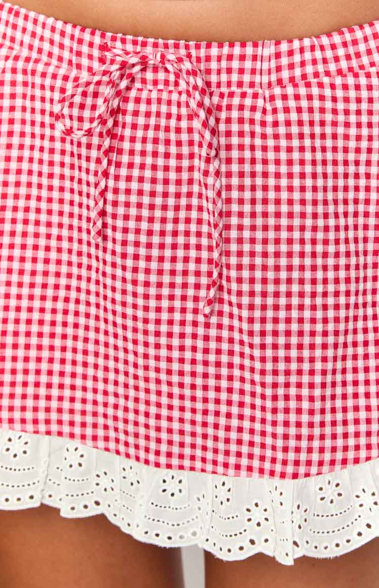 Close-up of the red gingham mini skirt showing the drawstring waist and white broderie anglaise hem