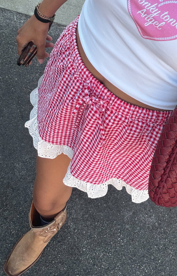 Close-up of the red gingham mini skirt showing the elasticated tie-front waist and white broderie anglaise ruffle hem