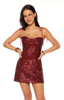 Our model wearing a dark red sequin mini-dress with a sweetheart neckline featuring a subtle quilted pattern on the bodice and thin tie-up shoulder straps.