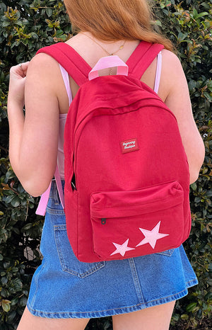 A red backpack with a front zippered pocket and two large white star appliques on the bottom. 