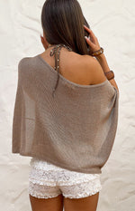 Rear view of a taupe metallic knit poncho with a draped off-shoulder neckline and a polka dot halter tie at the back