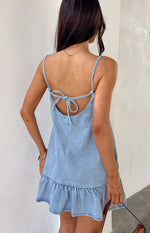 Rear view of a mid wash denim mini dress showing the low scoop back with a tie-back bow and ruffled hem