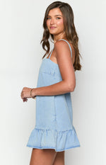 Side view of a mid wash denim mini dress with a square neckline, thin straps, side pocket, and ruffled hem