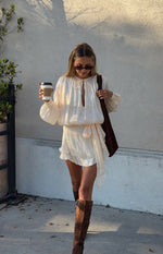 Pearl satin long sleeve mini dress with a tie neckline, elasticated waist, and a ruffled asymmetrical skirt with a long tie detail