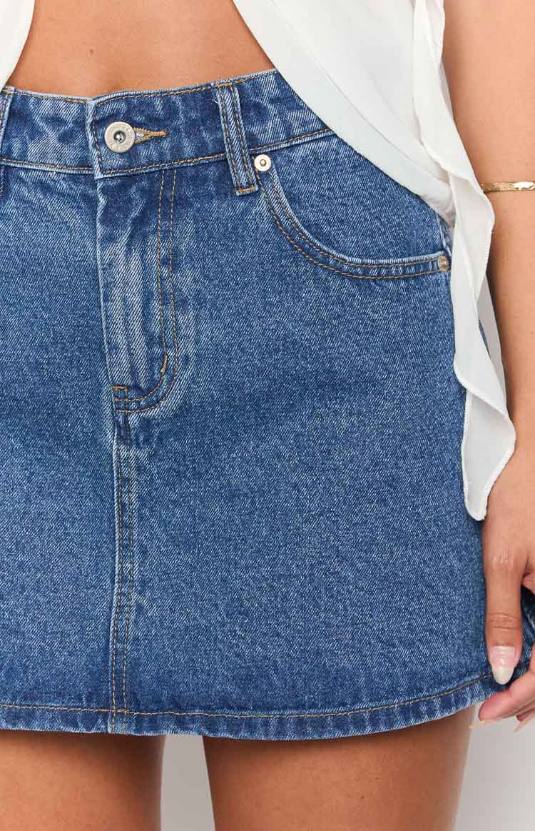 Close-up of the mid wash denim mini skirt showing the button closure, belt loops, and front pockets with contrast stitching