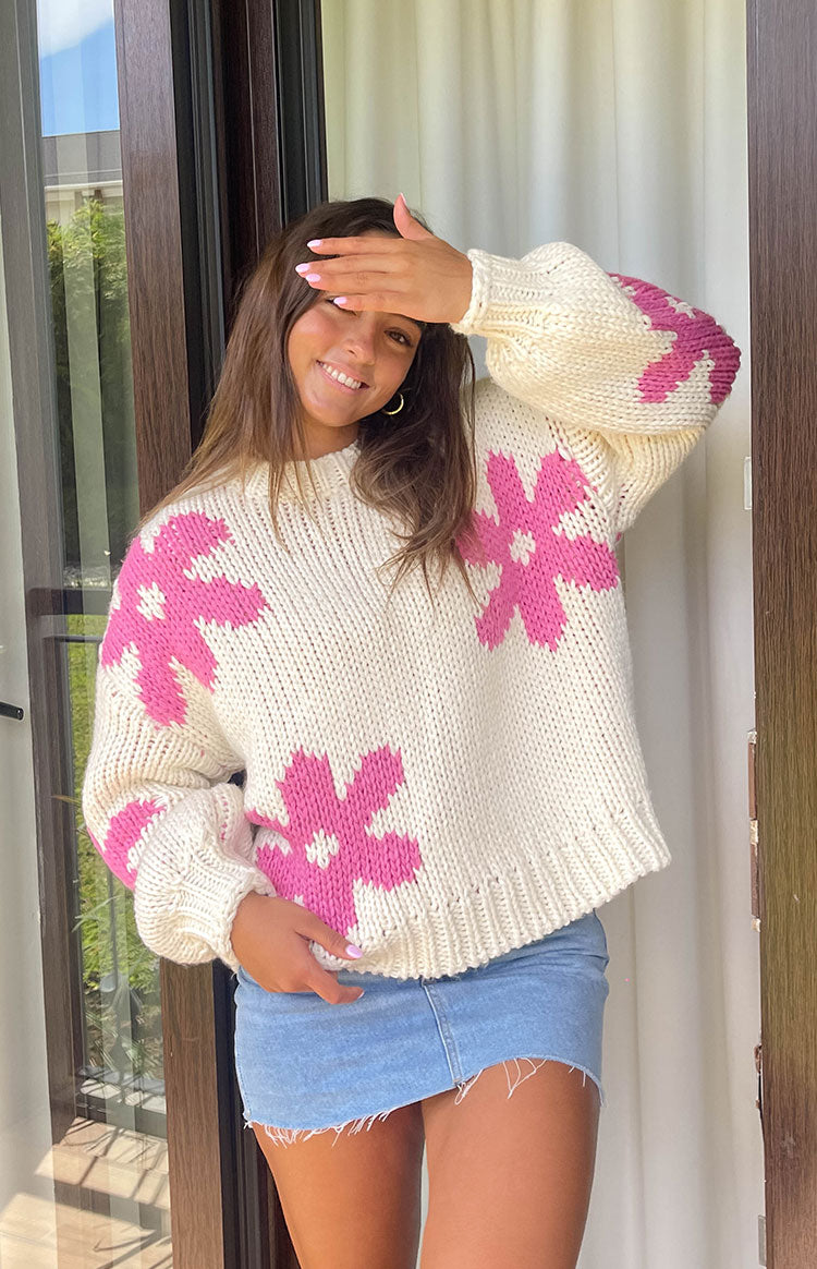 Cream knit sweater with large pink flower motifs on the body and sleeves, featuring a relaxed fit and ribbed hem