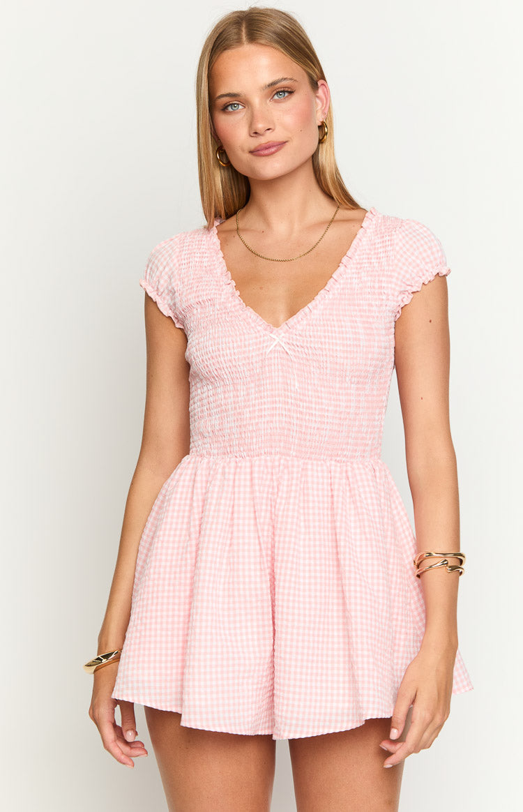 Front view of a pink gingham playsuit showing the smocked V-neck bodice with a small white bow and ruffled cap sleeves