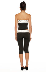 Angled front view of a black strapless top with white polka dot bands at the bust and hem, midriff cutout