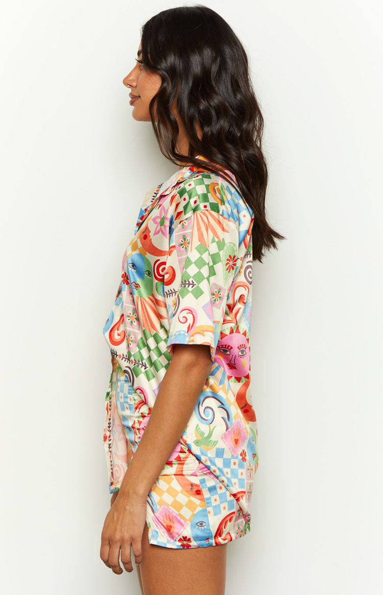 Side view of a vibrant abstract print satin shirt with short sleeves, a relaxed fit, and a side split hem