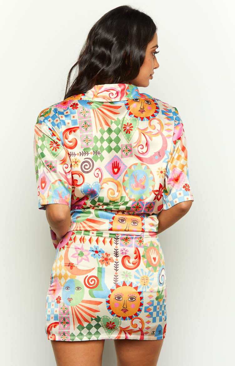 Back view of a fitted multi-coloured satin mini skirt with a vibrant resort print of suns, moons, and geometric shapes