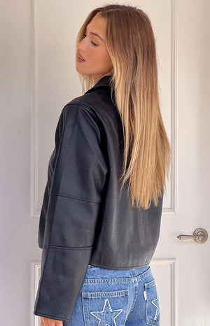 Side view of the black pebbled PU cropped jacket showing the hemline and seamed sleeves