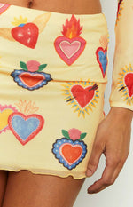 Close-up of the yellow mesh mini skirt with colourful sacred heart prints and a lettuce hem