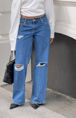 Full length view of mid wash blue straight leg jeans with large rips at both knees