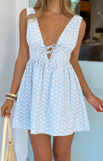 Front view of a blue gingham mini dress with white floral print, deep V-neck, lace-up bust tie, and shirred waist