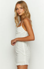 Side view of a white broderie mini dress with a square neckline, ruched side detail, and ruffled hem
