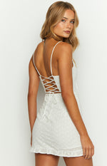 Rear-side view of a white broderie mini dress with a lace-up back, thin straps, and ruffled hem