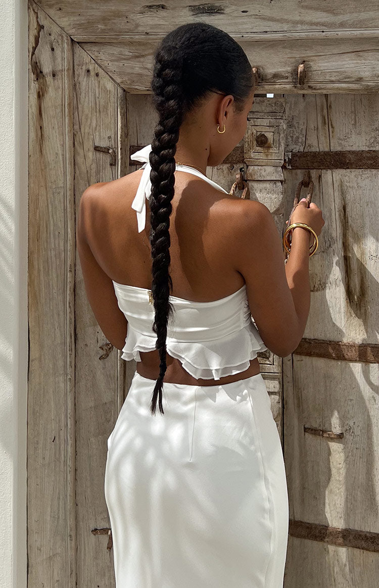 Rear view of a white chiffon crop top with a halter neck tie, exposed zipper, and ruffled hem