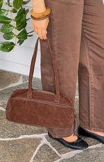 Close-up of a brown suede baguette bag showing the silver zipper and piping detail