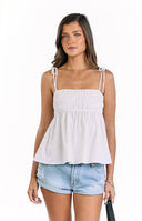 A white ruched top with adjustable tie-shoulder straps and a peplum-style hem- paired with light wash distressed denim shorts