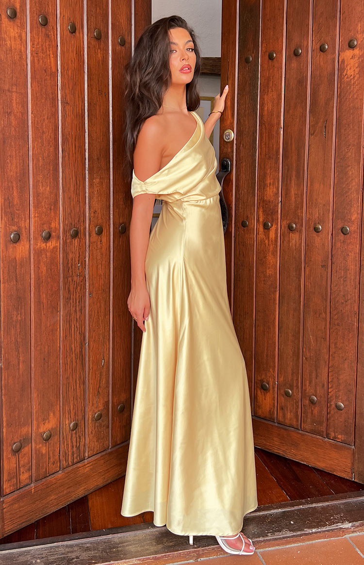 Side view of a yellow satin maxi dress with a draped one-shoulder neckline and flowy skirt