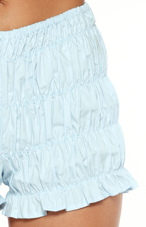 A lifestyle shot of our model wearing high-waisted light blue shorts. These shorts feature multiple horizontal tiers of gathered ruffles and an elasticized waistband.