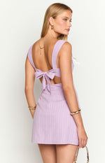 Rear view of a lilac mini dress with a tie-back bow, side waist cutouts, and subtle vertical stripes