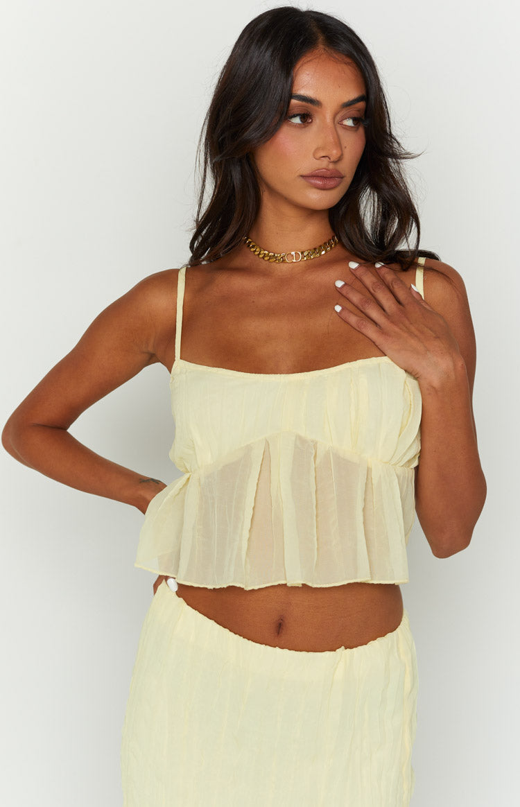 Close-up of a yellow cami top with thin spaghetti straps, gathered bust, and sheer crinkled peplum hem