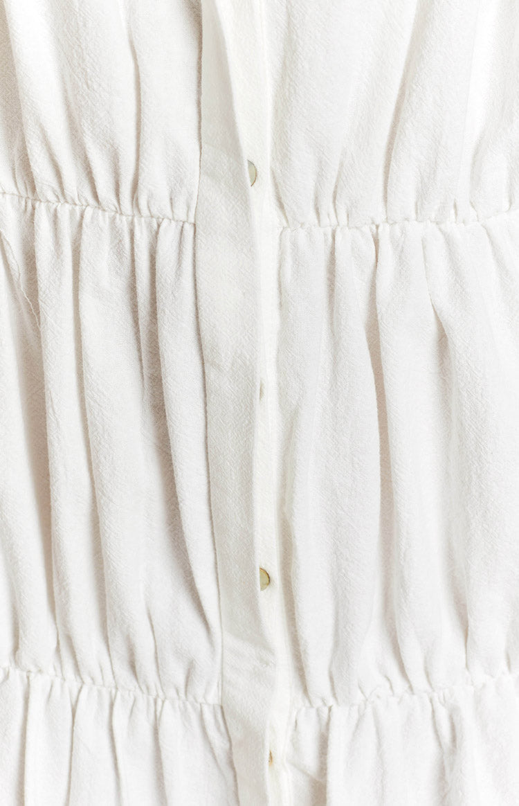 White textured dress with a button-front placket, shirred waist, and gathered tiers
