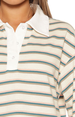 Close-up of the cream polo shirt's white collar, three-button placket, and horizontal teal and pink stripes