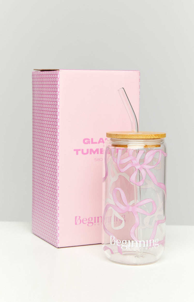 Front-right view of clear glass tumbler with scattered pink bow pattern, bamboo lid, and bent glass straw