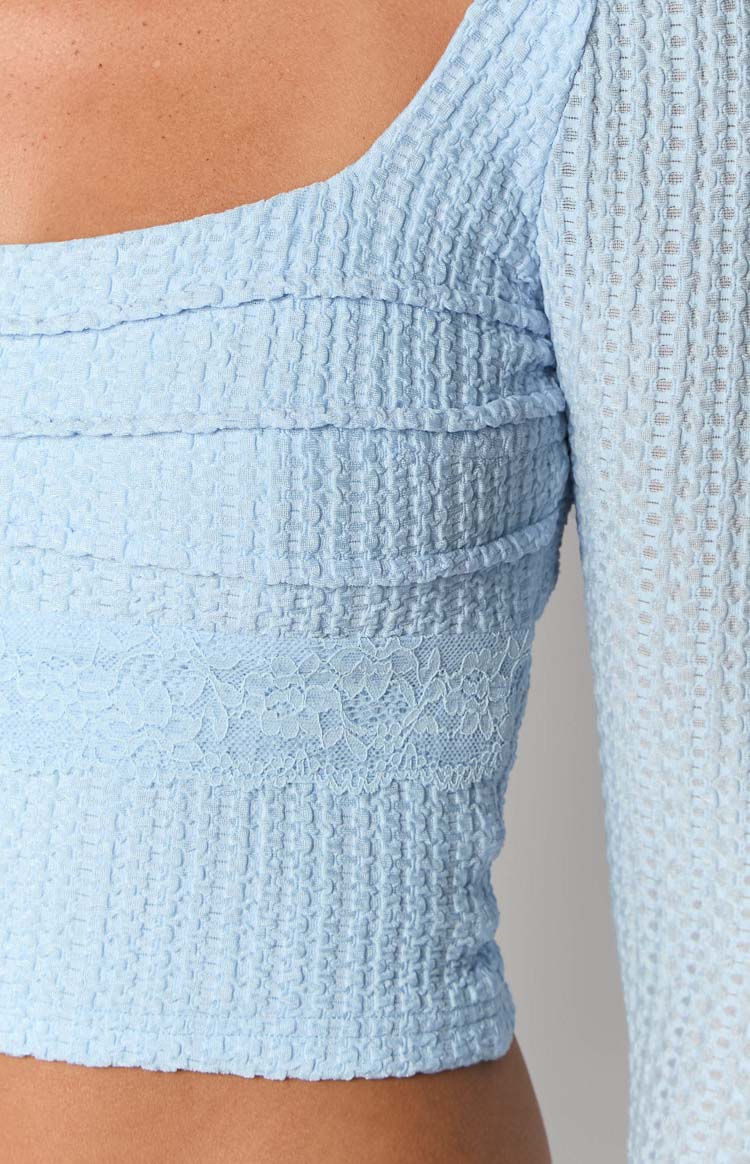 Detail shot of the light blue long sleeve top featuring textured fabric, horizontal ruched bands, and a floral lace panel