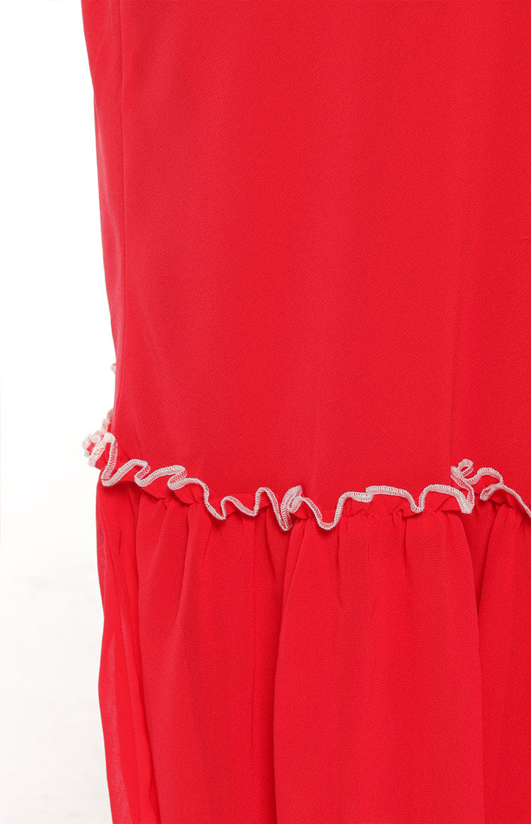 Close-up showing the white zigzag ruffled trim detail along the hem of a red maxi skirt