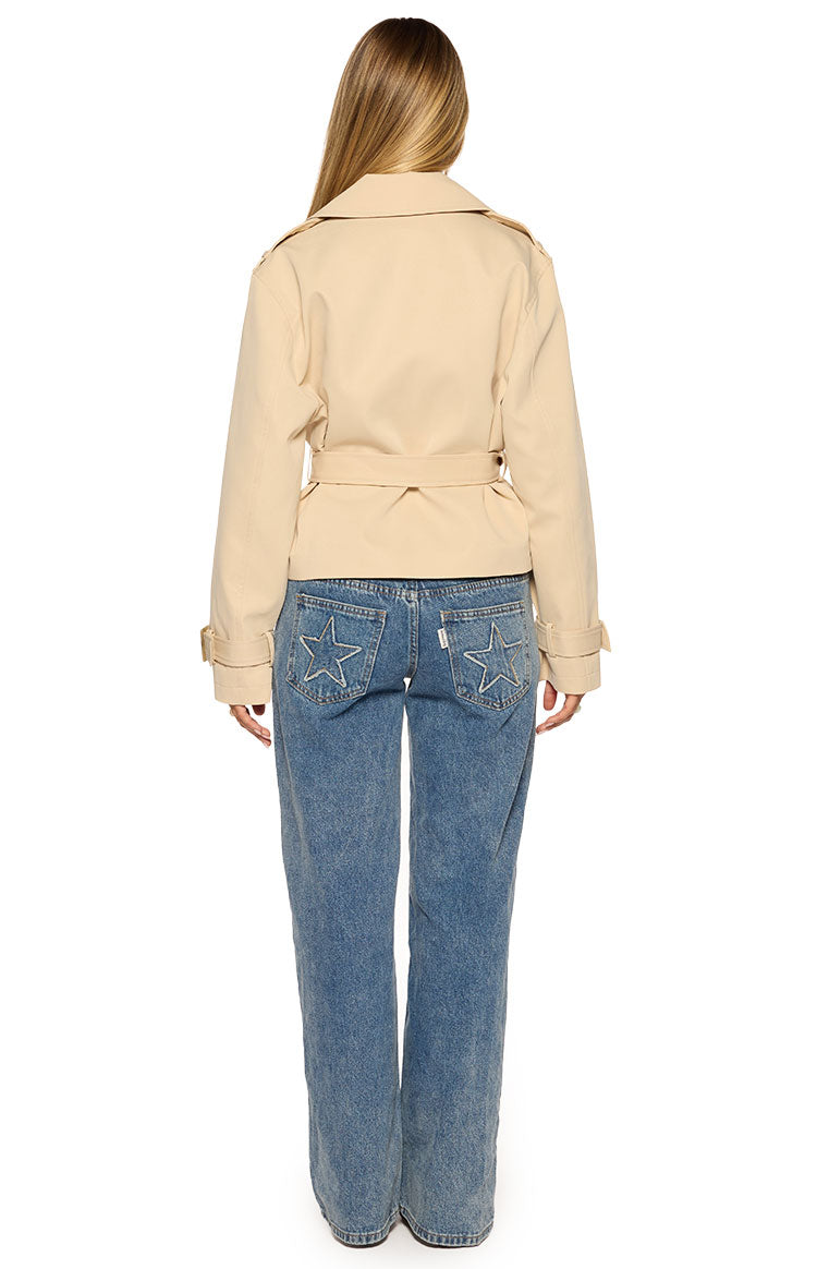 Rear view of a cream cropped trench coat with a belted waist and storm flap details