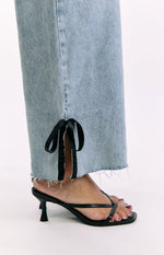 Close-up of the raw-cut hem of light wash denim jeans with a side slit tied by a black satin bow