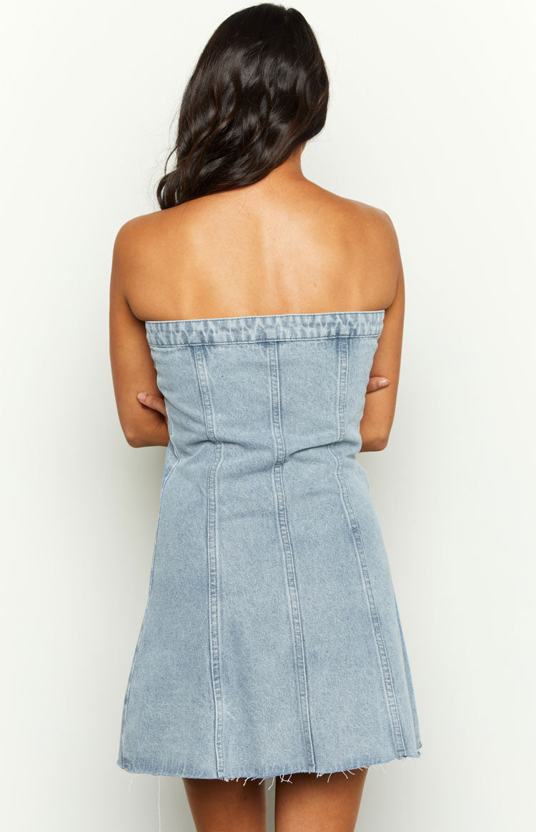 Back view of a light wash denim strapless mini dress featuring visible corset boning seams and a frayed hem
