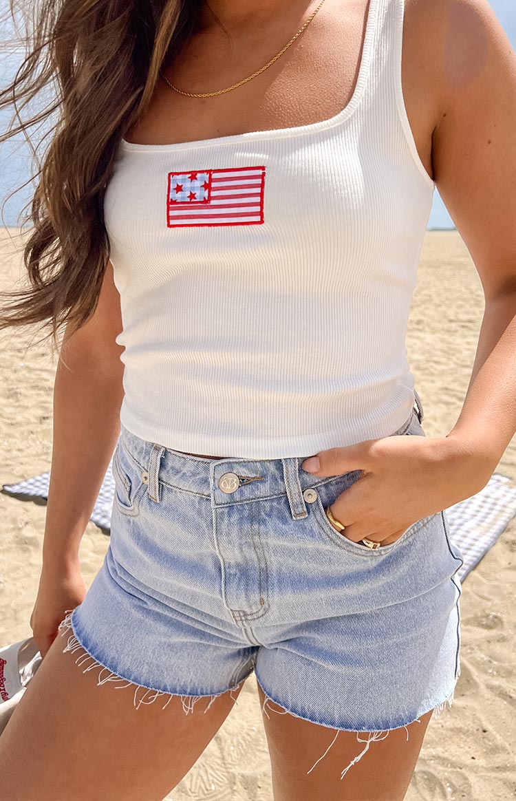 Model wearing light wash denim shorts with a raw edge hem paired with a white graphic tank